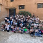 مجموعة كبيرة من الأطفال، أولاد وبنات، يجلسون في ساحة المدرسة ويحملون شهادات مشاركة في يوم كشفي.