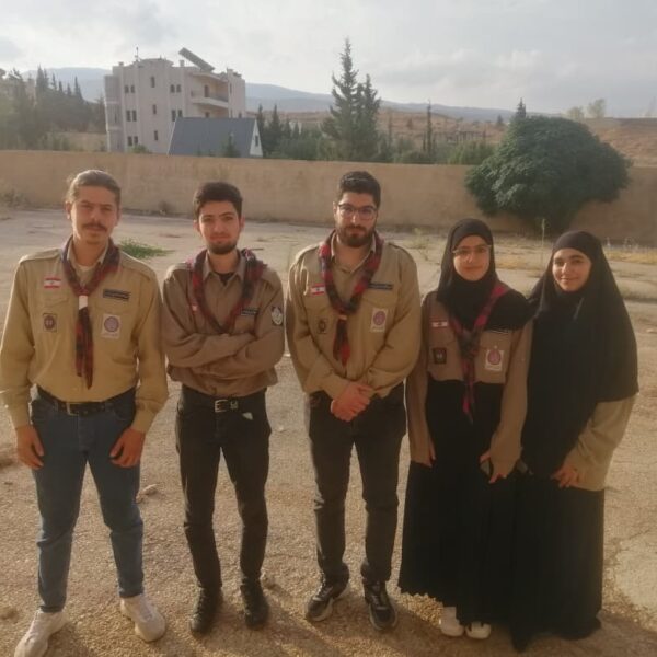 مجموعة من الشباب والشابات يرتدون زي الكشاف ويقفون معاً في ساحة المدرسة.