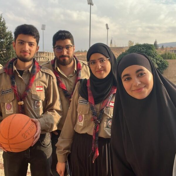 مجموعة من الشباب والشابات يرتدون زي الكشاف ويقفون معاً في ساحة المدرسة.